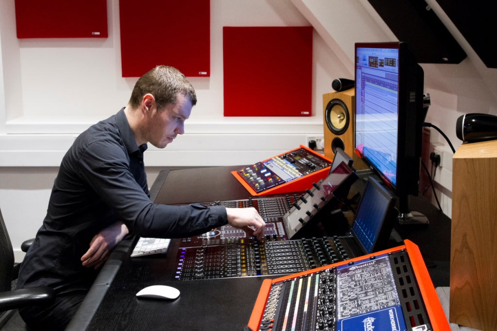 Person sitting at a mixing console with small GIK panels on the wall
