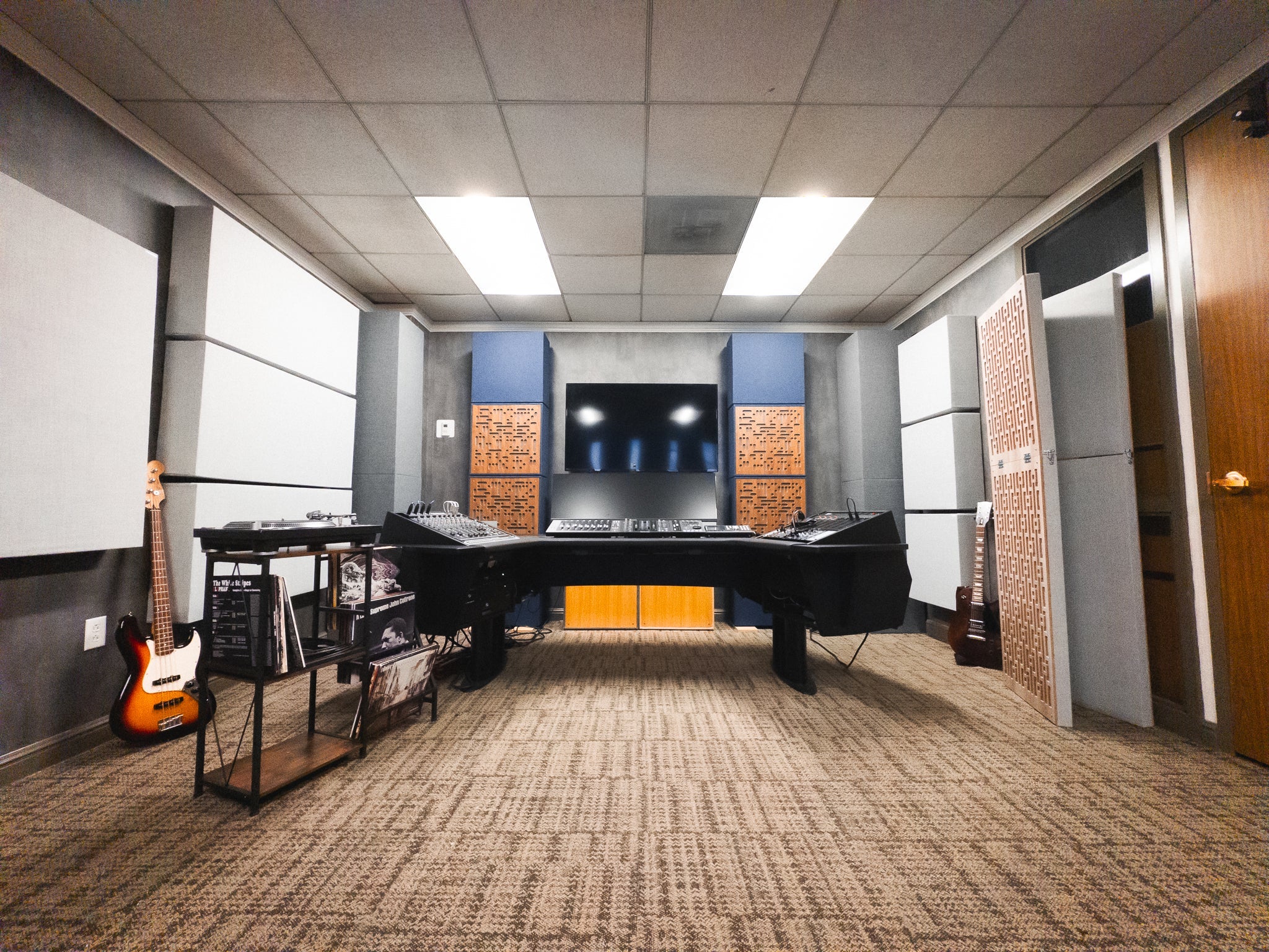 Recording studio control room with GIK Acoustics acoustic panels on the walls and ceiling, featuring a mixing desk, studio monitors, and Amplitude™ acoustic panels in orange and natural wood finishes on the rear wall.