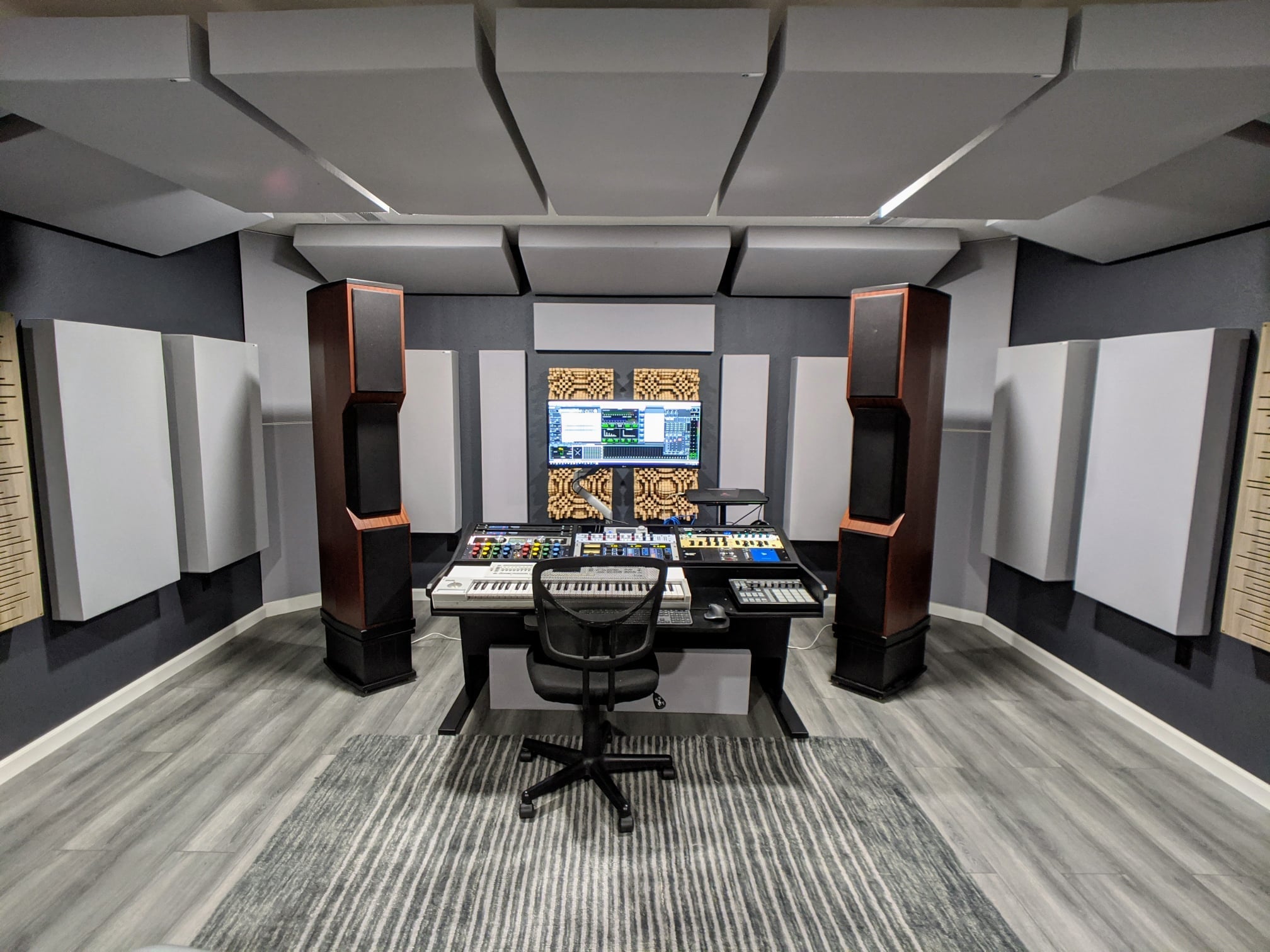 Recording studio mix position with GIK Acoustics acoustic panels on walls and ceiling, Gotham Primitive Root Diffusers on the rear wall, and large floor-standing speakers.